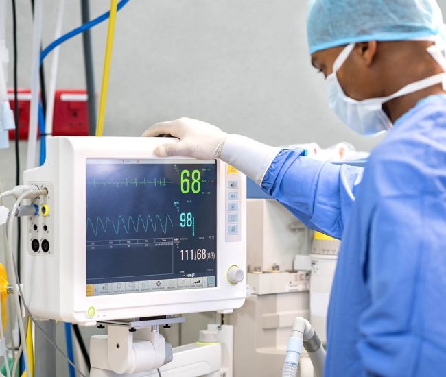 African surgeon keeping track of vital functions of the body during cardiac surgery. Surgeon looking at medical monitor during surgery. Doctor checking monitor for patient health status.